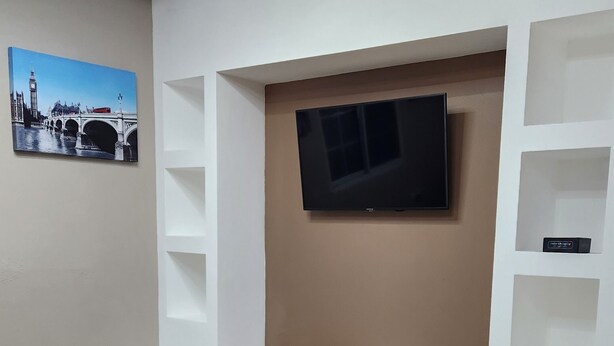 Ein modernes Wohnzimmer mit einem an der Wand montierten Flachbildfernseher, einem schwarzen Sofa und einer Holzeinbauwand mit Regalen.