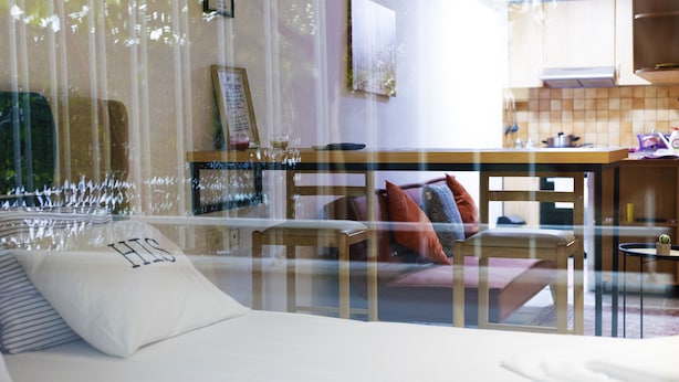 A room with a bed, a chair, a table, and a view through a window. - Atomium Apartments (Tirana)