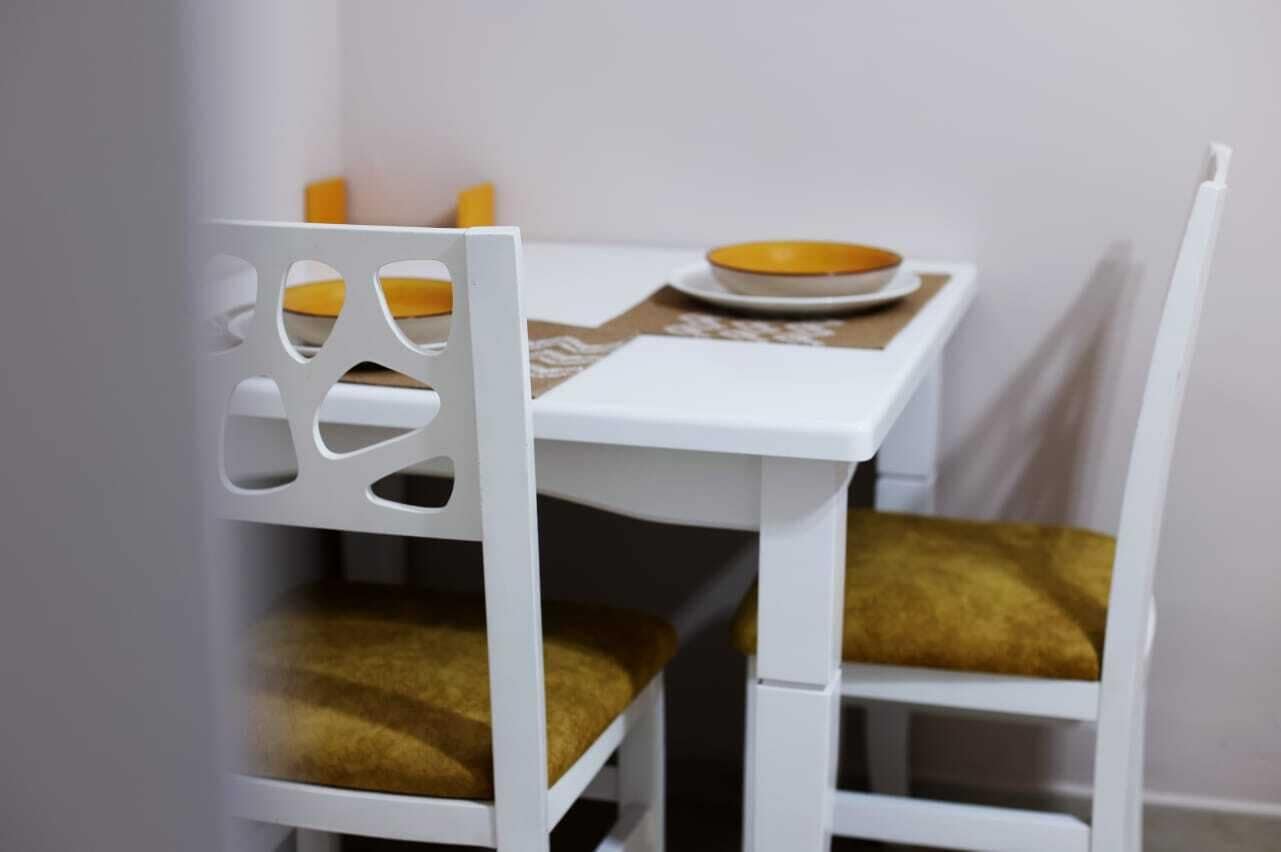 A white dining table with a yellow bowl and a plate on it, accompanied by a white chair with a gold cushion.