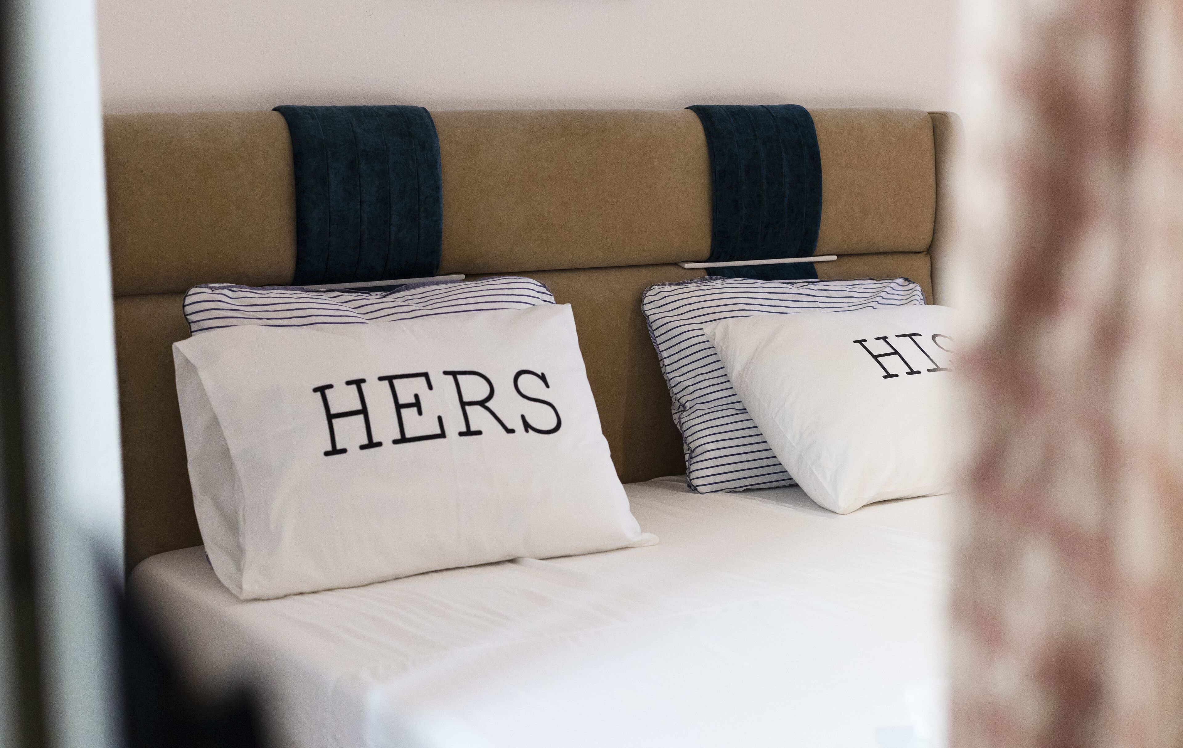 Una cama con dos almohadas, una con la etiqueta 'HERS' y la otra con la etiqueta 'HIS'.