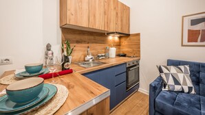 A modern kitchen with wooden cabinets, a sink, and a stove. There is a dining table with blue plates and a red napkin. A blue sofa is in the corner. - Atomium Apartments (Tirana)