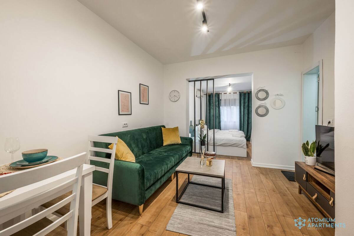 A modern living room with a green sofa, a dining table with chairs, a coffee table, and a TV on a wooden cabinet.