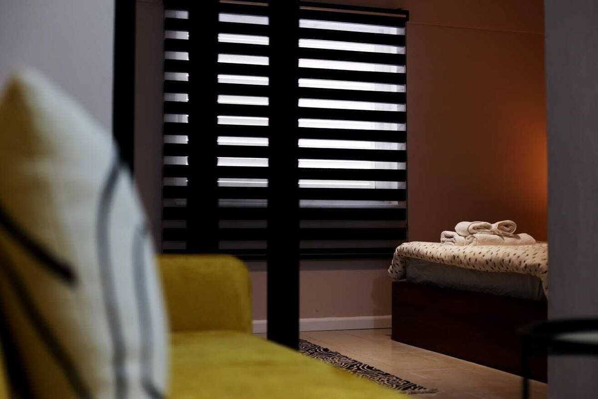 A room with a bed, a yellow chair, and a window with blinds.