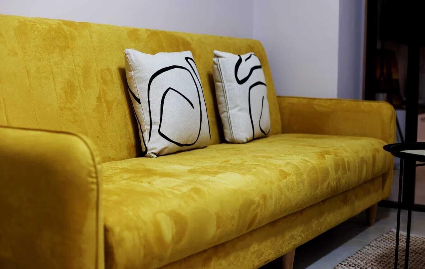 Un canapé jaune agrémenté de deux coussins blancs ornés de motifs abstraits noirs.