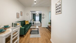 A modern living room with a green sofa, a white coffee table, and a dining area with a white table and blue bowls. - Atomium Apartments (Tirana)