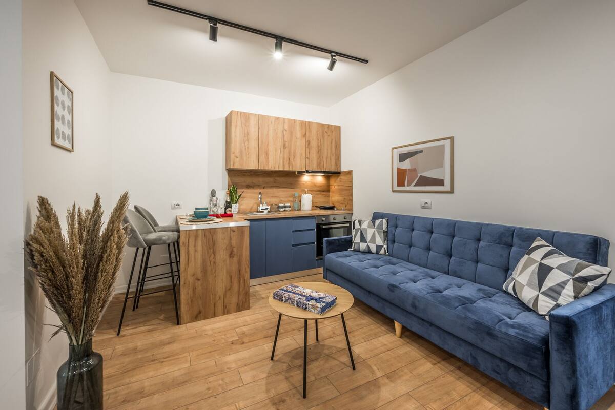 A compact living space with a kitchenette, a blue sofa, a small round table, and a decorative vase.