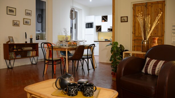 A living room with a sofa, a coffee table with mugs, a dining area with chairs and a table, and a kitchen in the background. - Proche DU Vieux Port AU Calme (Marseille)