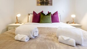 A neatly made bed with white towels, a green and pink pillow, and two bedside lamps.
