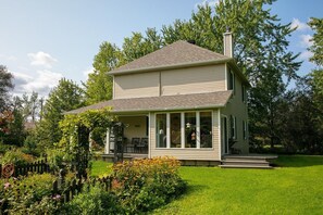 A two-story house with a covered porch, surrounded by a well-maintained garden and trees.
