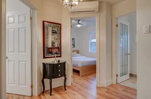 A hallway with a bed, a small table, and a door leading to a bedroom.