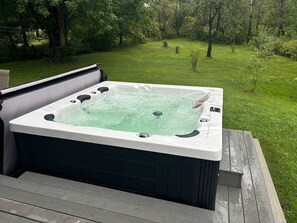 A hot tub on a wooden deck with a grassy yard in the background.