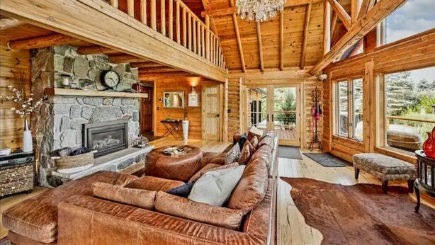 A log cabin interior with a stone fireplace, leather sofa, and a chandelier.