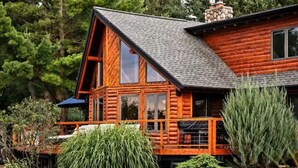 A log cabin with a large deck, a chimney, and a stone fireplace.