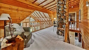A cozy log cabin interior with a high ceiling, a stone pillar, a sofa, and a dining area.