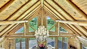 A log cabin with a high gable roof, large windows, and a chandelier.