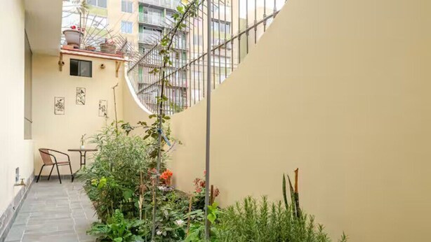 A narrow courtyard with a tiled floor, a small table and chair, and various plants and flowers. - Hermoso y Tranquilo Loft con Netflix Incluido (Lima)