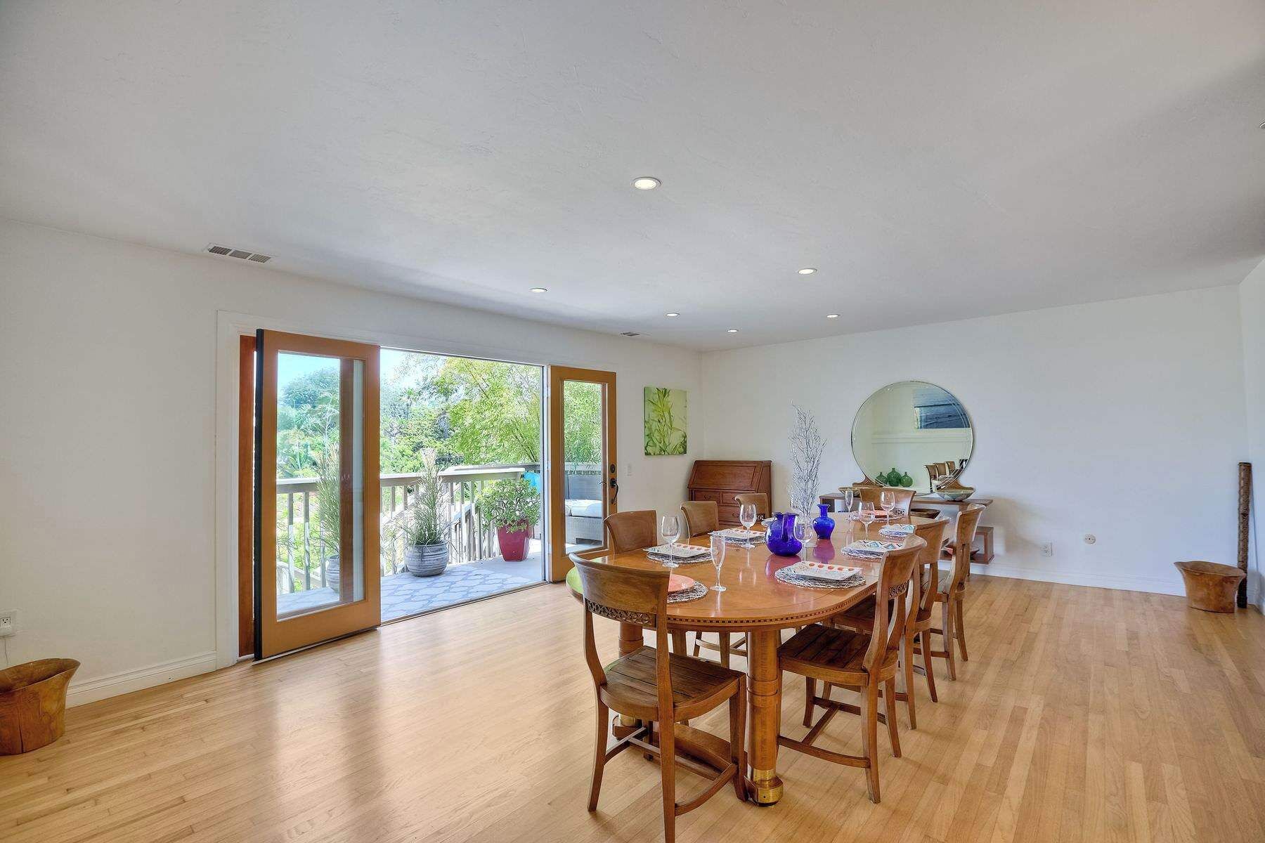 A spacious dining area with a wooden table and chairs, a large mirror, and a view of greenery through the sliding glass doors.