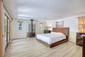 A spacious bedroom with a large bed, a wooden floor, a decorative wall piece, and a fireplace.