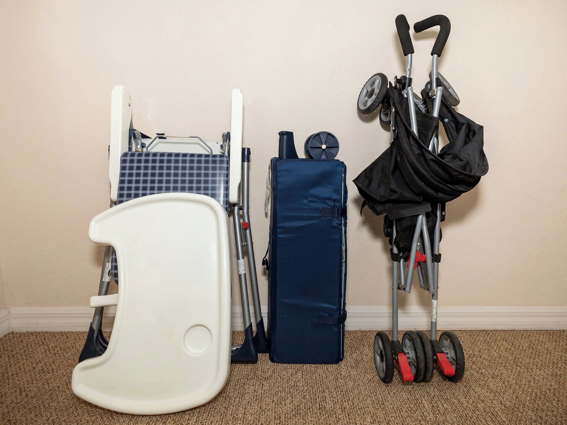 Une pièce avec une chaise blanche, une chaise pliante bleue, une boîte de rangement bleue et une poussette, le tout adossé à un mur beige.