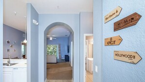 A modern interior with a kitchen, dining area, and a hallway leading to a living room. There are wooden signs on the wall indicating distances to various locations. - Dreamers Oasis At Bahama Bay Sleeps 8! (Davenport)