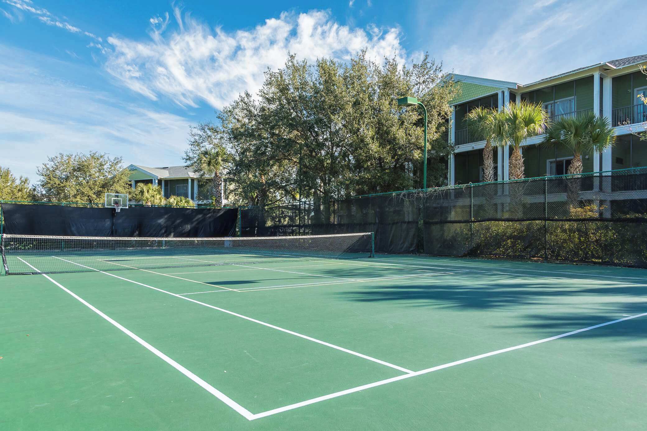 Un campo da tennis con una rete, circondato da una recinzione e alberi.