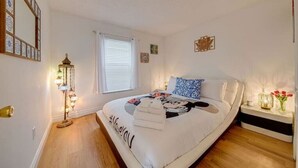 Quarto com cama, mesa de cabeceira, abajur e janela com persianas.