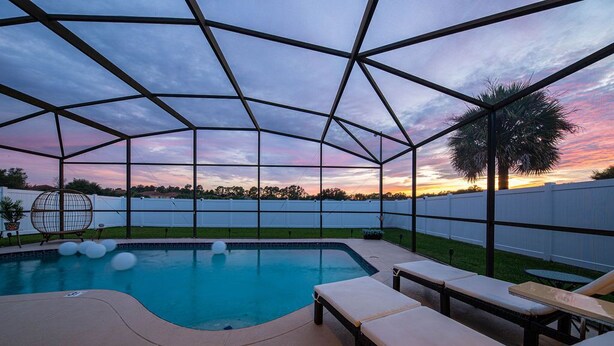 Piscina ao ar livre coberta com espreguiçadeiras e vista para o pôr do sol.