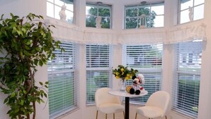 Quarto nos cantos com janela saliente, duas cadeiras brancas, uma mesinha com um vaso de flores e uma figura de Mickey Mouse.