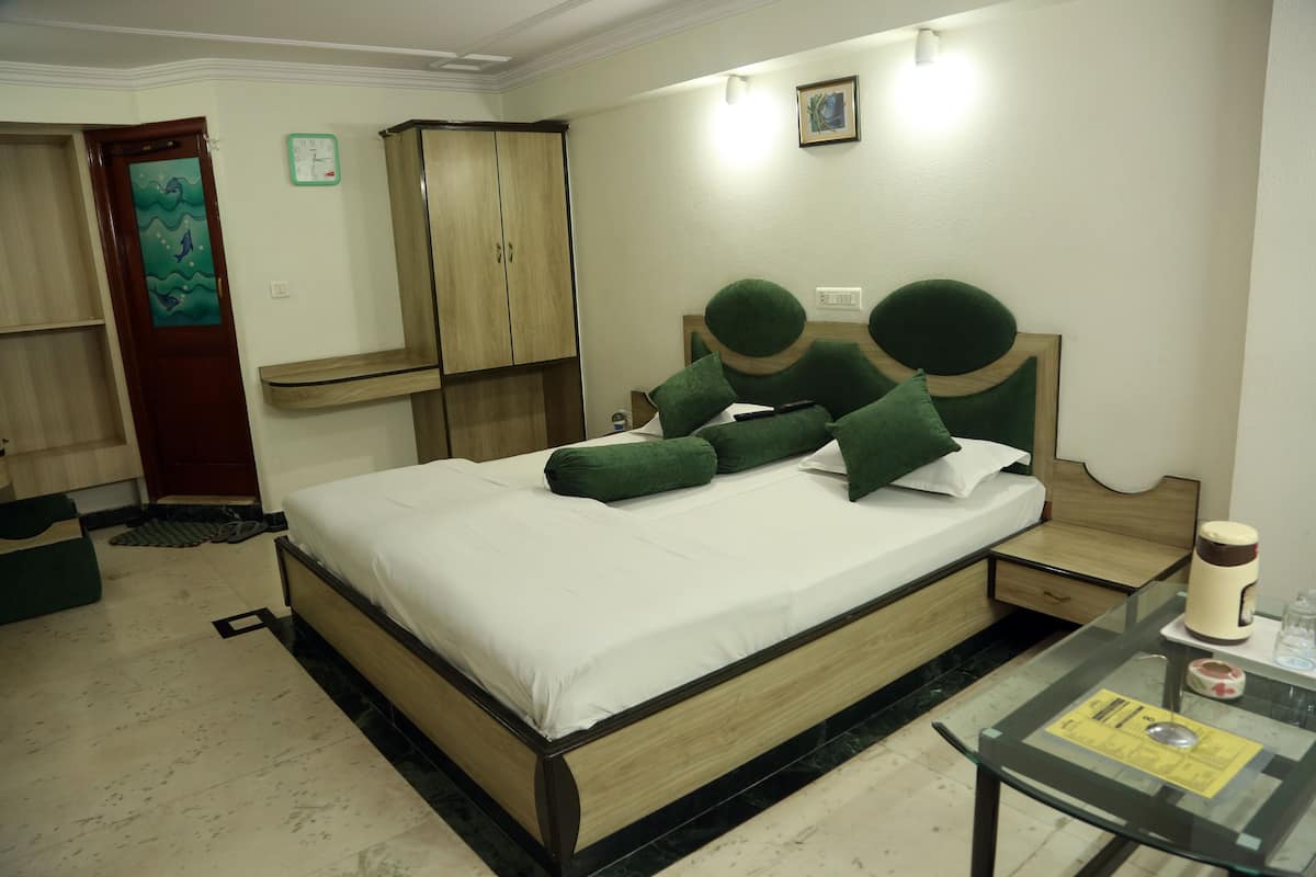 A hotel room with a bed, a nightstand, a glass table, a wardrobe, and a clock on the wall.
