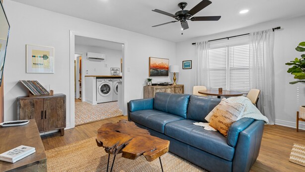 A modern living room with a blue leather sofa, a wooden coffee table, and a ceiling fan. - Mid-City Bungalow, 1 Mile from Bathhouse Row, Pup Friendly, Fully Fenced Yard! (Hot Springs)