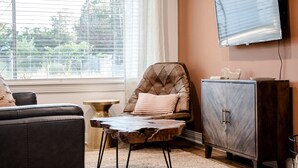 A living room with a leather sofa, a wooden coffee table, a cushioned chair, a cabinet, and a television mounted on the wall. - Mid-City Bungalow, 1 Mile from Bathhouse Row, Pup Friendly, Fully Fenced Yard! (Hot Springs)