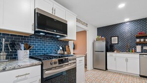A modern kitchen with white cabinets, a stainless steel stove, and a blue-tiled backsplash. - Mid-City Bungalow, 1 Mile from Bathhouse Row, Pup Friendly, Fully Fenced Yard! (Hot Springs)