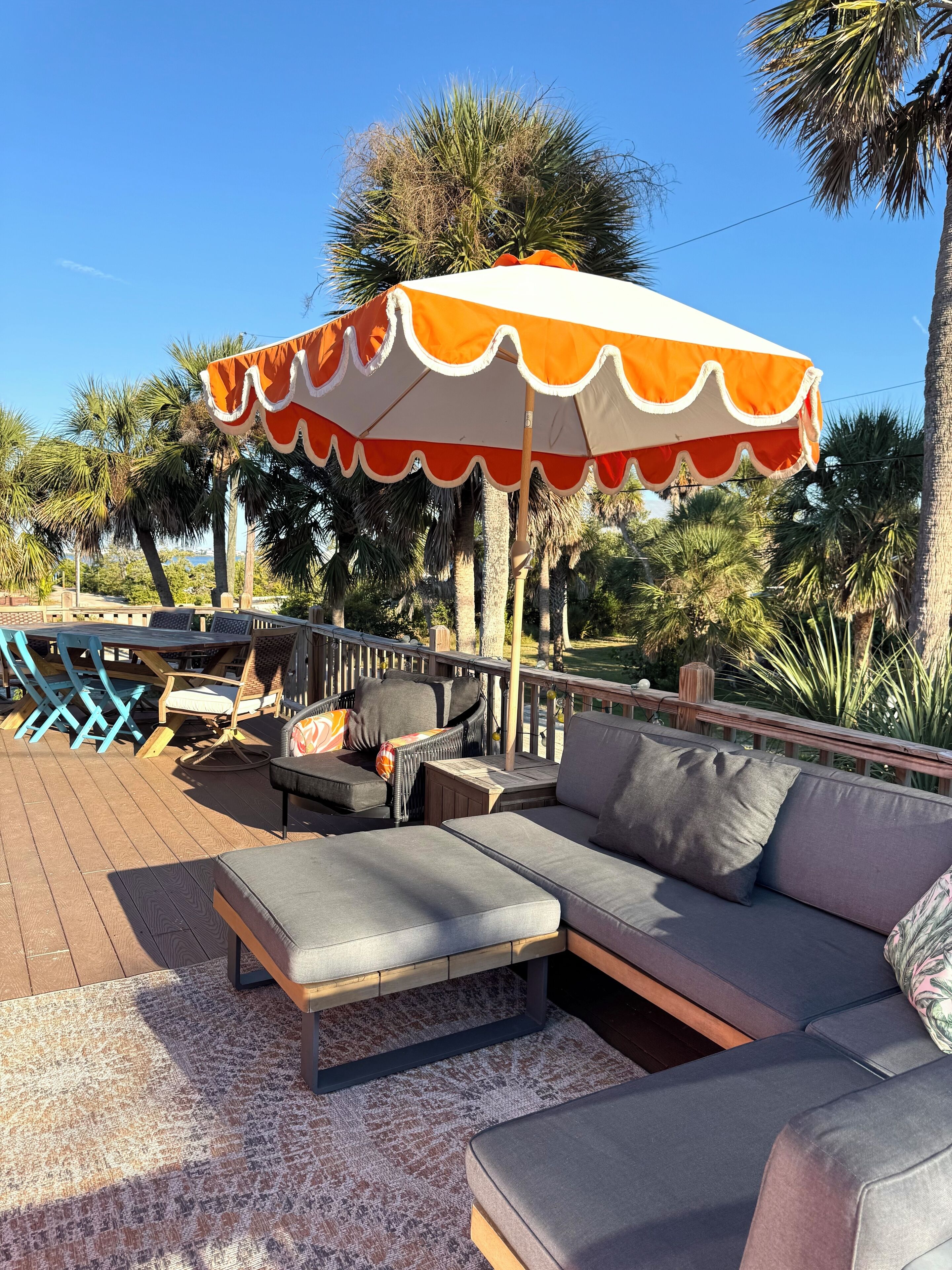 A deck with a sectional sofa, a patterned rug, and a large umbrella.