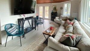 Ett rymligt vardagsrum med ett träpanelat tak, en platt-TV som är monterad på väggen, en soffgrupp och en matplats med stolar och ett bord.