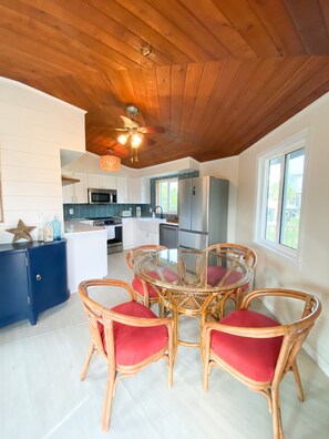 A modern kitchen with white cabinets, a central island, and a dining area with wicker chairs and red cushions.
