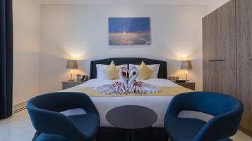 A modern hotel room with a large bed, two bedside lamps, a wall-mounted artwork, and a wooden wardrobe.