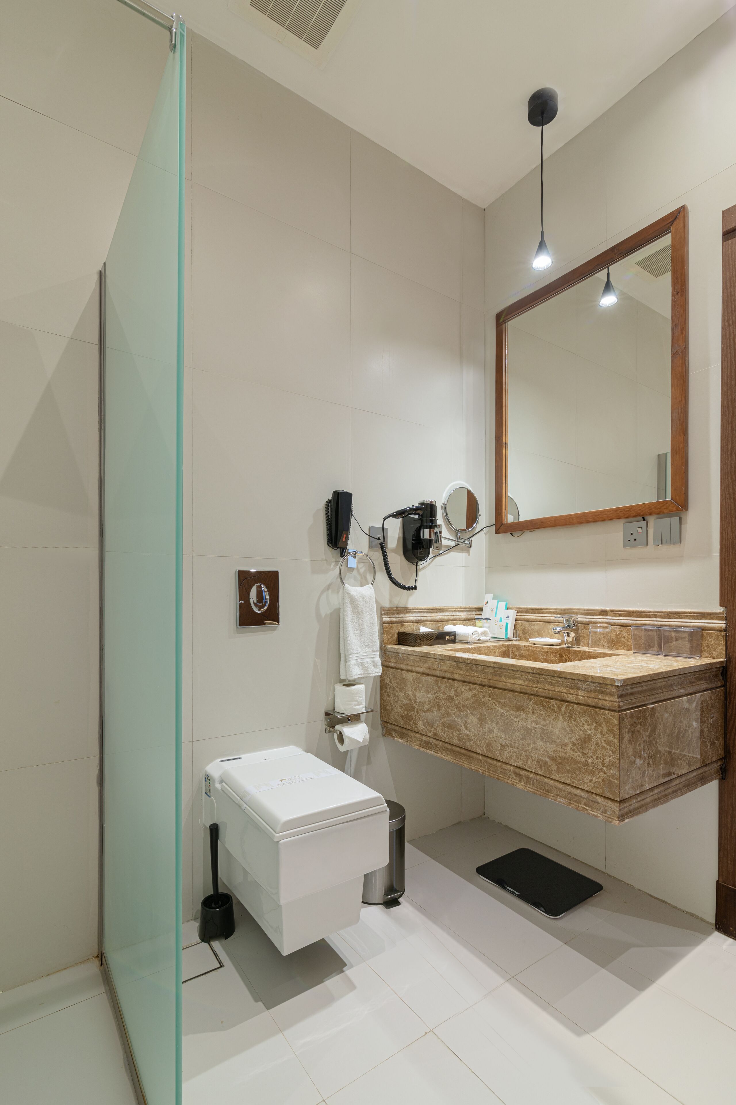 A modern bathroom with a glass shower enclosure, a vanity with a marble countertop, a large mirror, and a hairdryer on the wall.