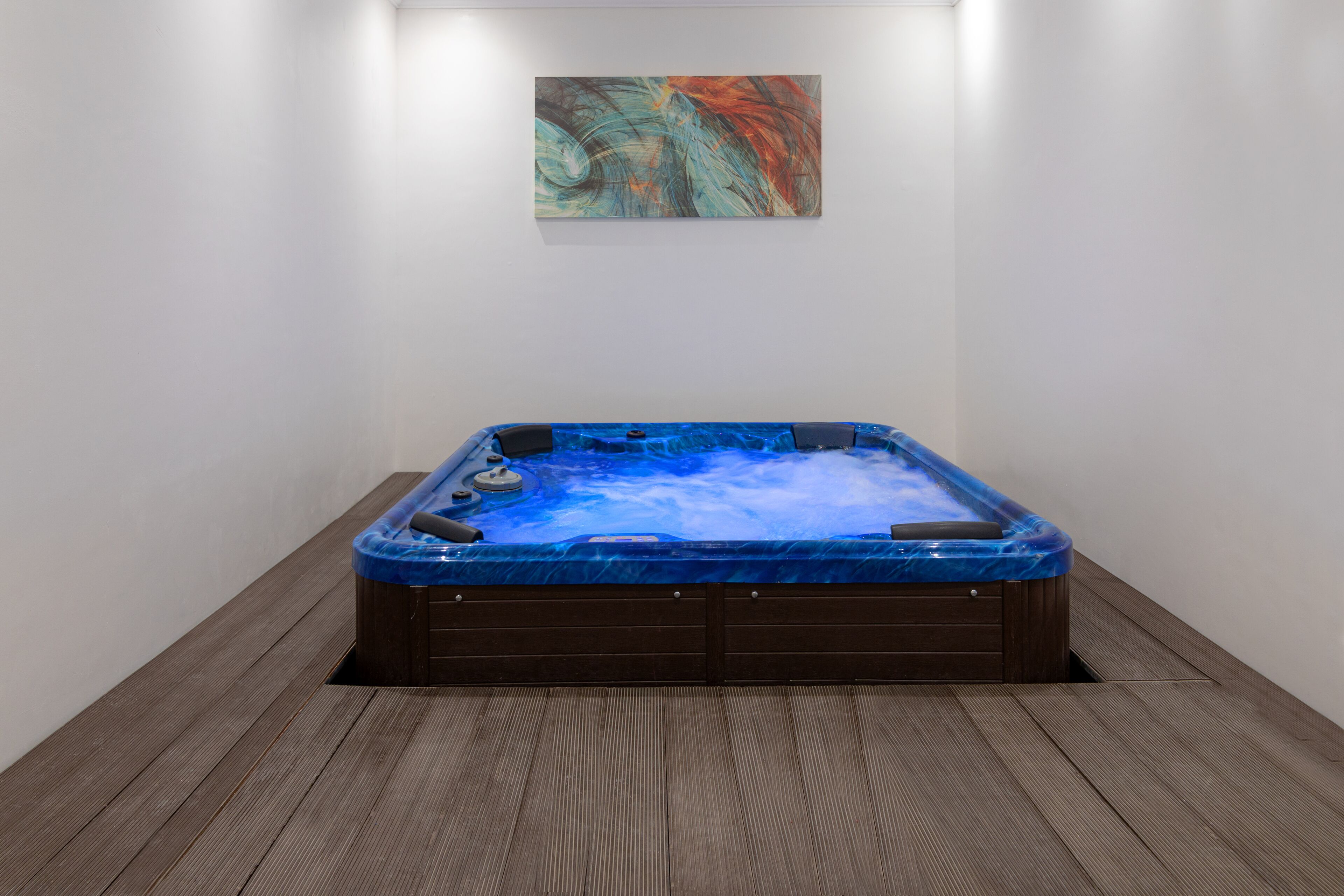 A hot tub in a room with wooden flooring and a single abstract painting on the wall.