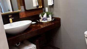 A bathroom with a wooden vanity, a white sink, a large mirror with a gold frame, and a towel rack with white towels.
