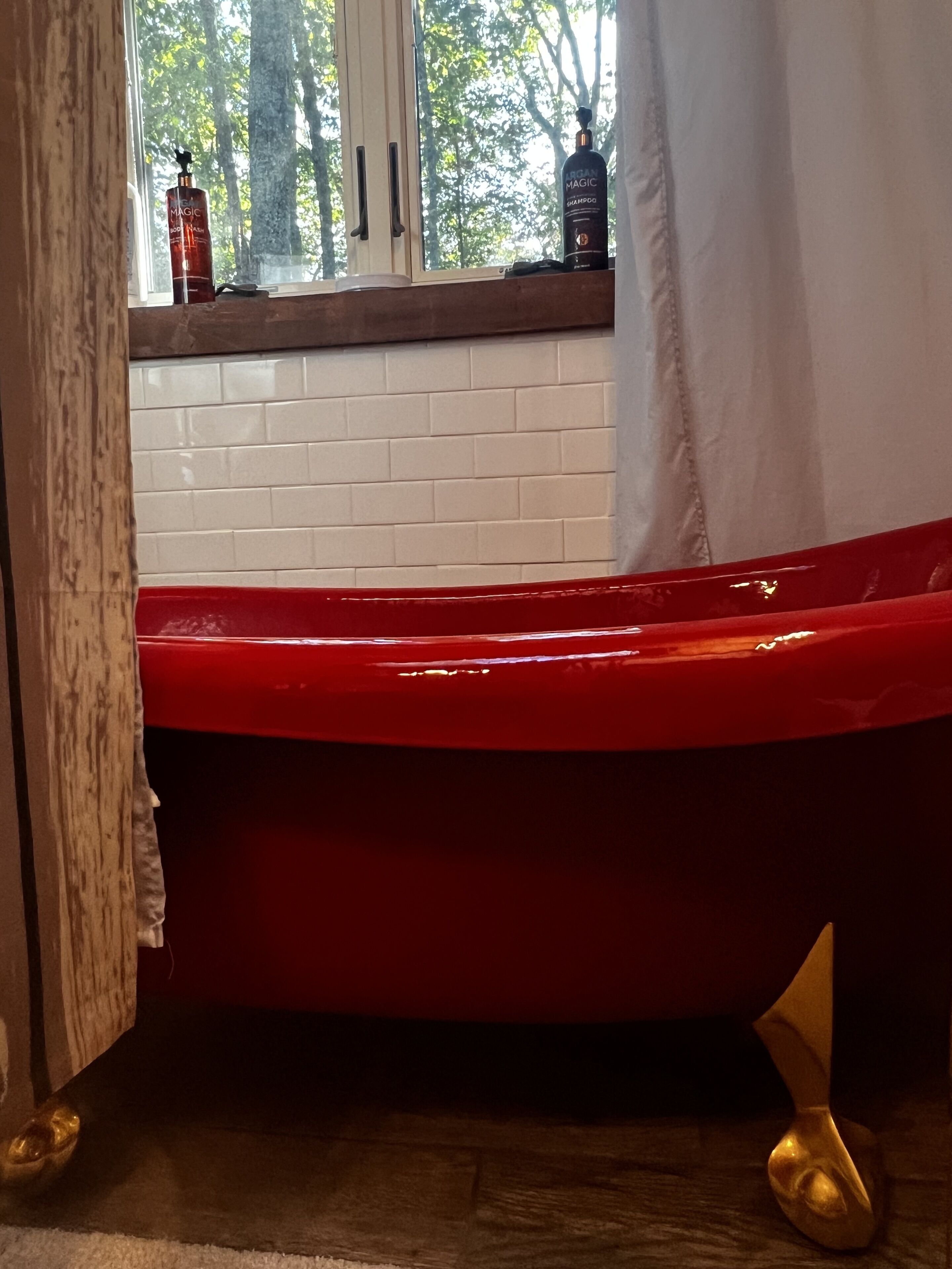 Een rood bad in een badkamer met uitzicht op bomen.