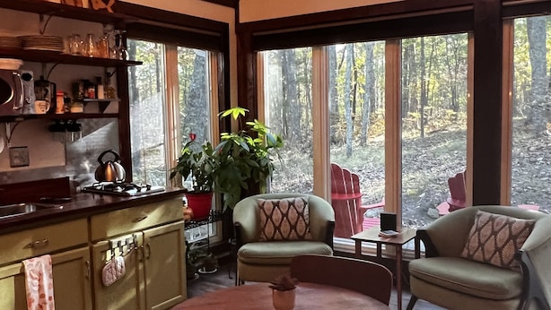 Interior acogedor de una cabaña con techo de madera, un comedor con mesa redonda y una cocina con pileta y alacenas.