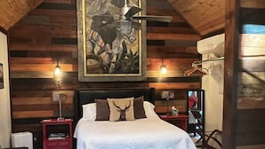Una habitación acogedora con una cama, una mesa redonda, un tapiz de cuero de vaca y un cuadro en la pared.
