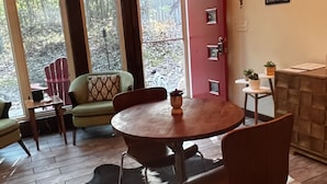 Una habitación acogedora con una mesa redonda de madera, dos sillas, una mesita de noche con una lámpara y una puerta roja.