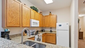 Eine Küche mit Granit-Arbeitsplatten, Holzschränken, einer Edelstahlspüle, einer Mikrowelle, einem Kühlschrank und einer Kaffeemaschine.