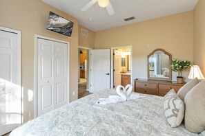 Quarto com cama, penteadeira, espelho e porta que dá para um banheiro.