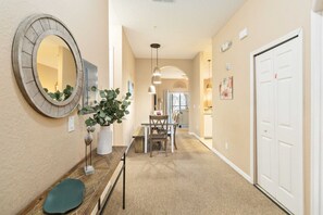 A hallway with a dining area, a round mirror, a potted plant, a bench, and a door.