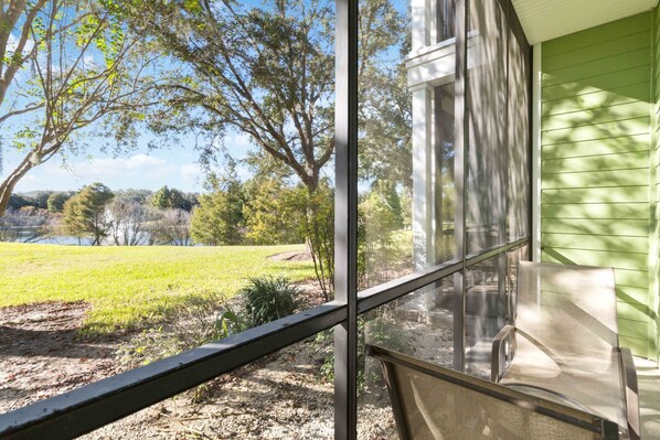 A view through a window with a metal railing, a green building, and a grassy area with trees.