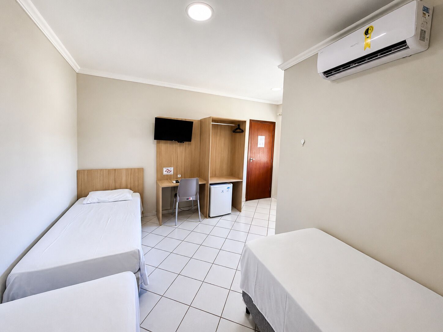Habitación de hotel con dos camas individuales, un escritorio con una silla, un televisor, un armario y un equipo de aire acondicionado.