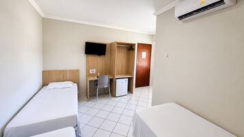 Habitación de hotel con dos camas individuales, un escritorio con una silla, un televisor, un armario y un equipo de aire acondicionado.