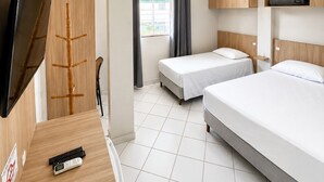 Habitación de hotel con dos camas, un televisor, un escritorio con silla, una ventana con cortinas y una repisa con una bolsa.